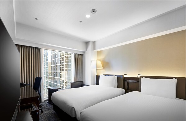 Ein Hotelzimmer mit zwei Betten, einem Schreibtisch, einem Stuhl, einer Lampe und einem großen Fenster mit Vorhängen.
