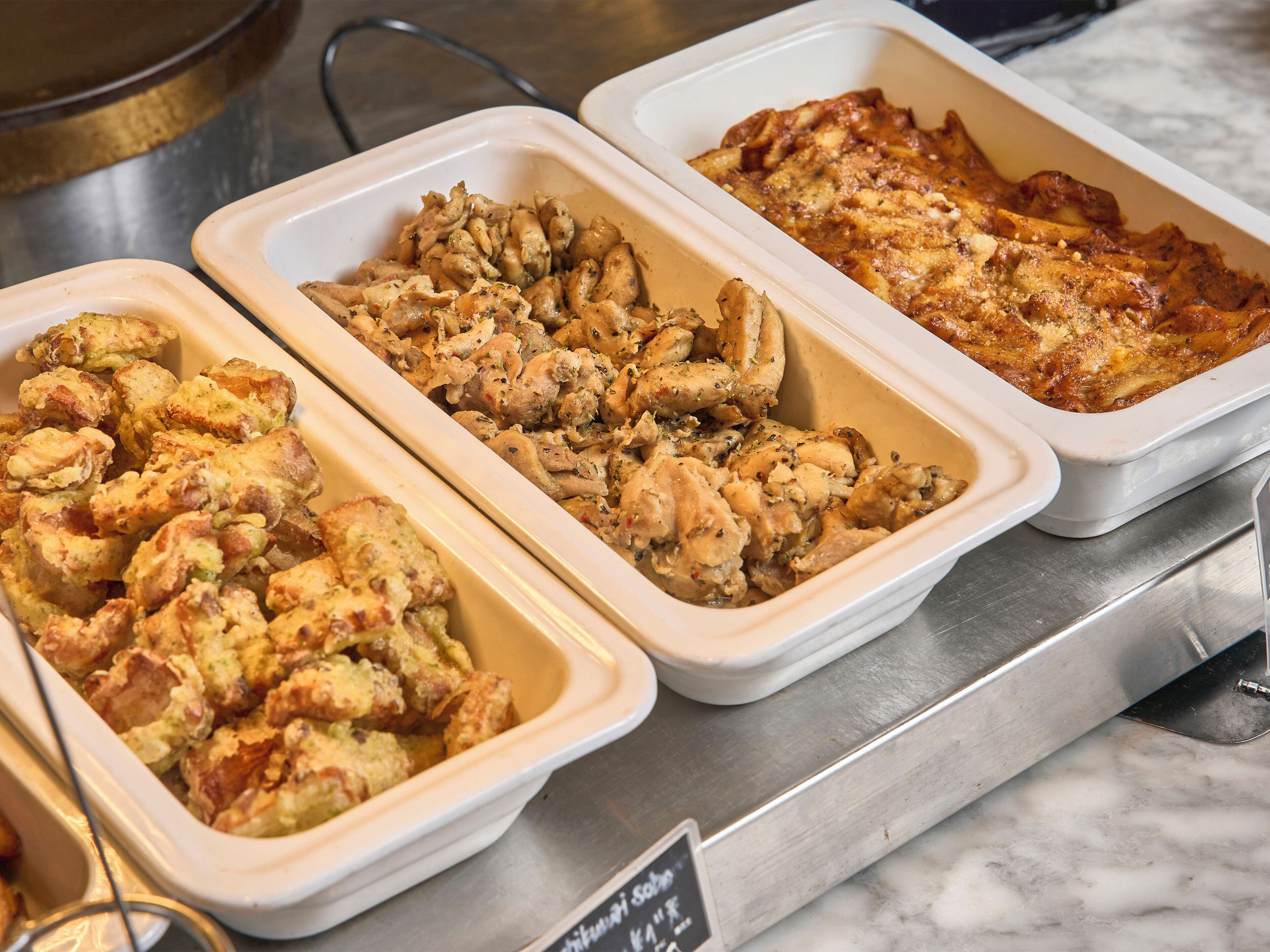 Three rectangular serving dishes containing different dishes, placed on a metal counter.