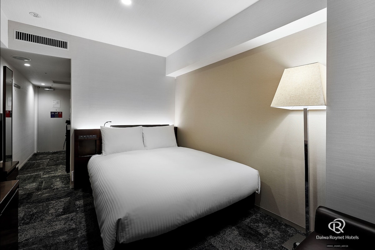 A hotel room with a bed, a nightstand, a lamp, and a carpeted floor.