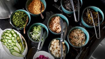 A variety of food items in bowls on a table, including sliced cucumbers, shredded greens, and other ingredients.