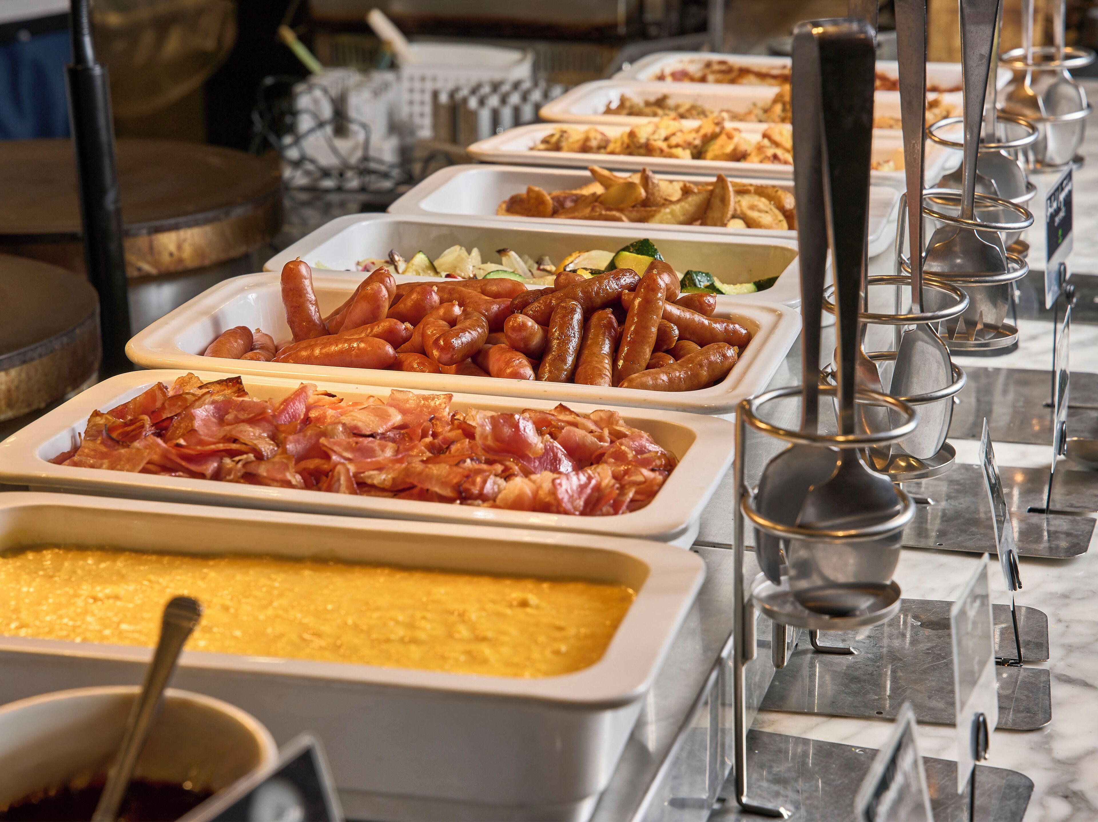 A buffet with various food items including sausages, bacon, and a casserole dish.