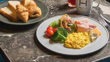 Colazione con croissant, insalata, uova strapazzate, prosciutto e un bicchiere di succo su un tavolo di marmo.