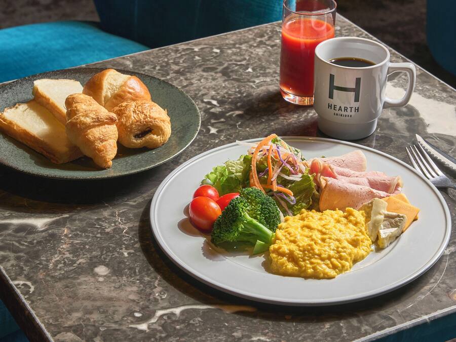 Colazione con croissant, insalata, uova strapazzate, prosciutto e un bicchiere di succo su un tavolo di marmo.