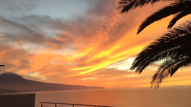 Una vista del tramont a un balcó amb vista a una piscina i al mar, amb una muntanya de fons.