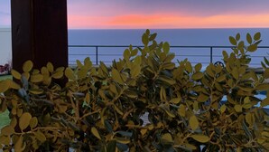 Un balcó amb vista al mar al capvespre, envoltat de vegetació.