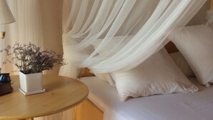 Un dormitori amb un llit, nujols blancs, una taula de nit amb una làmpada i una petita planta en test.