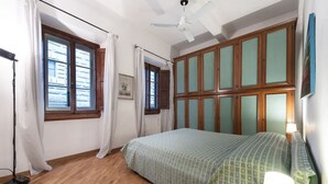 Ein Schlafzimmer mit Bett, Deckenventilator, Fenster mit Vorhängen und Heizkörper.