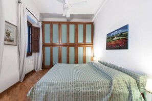 A bedroom with a bed, a window with curtains, a ceiling fan, and a painting on the wall.