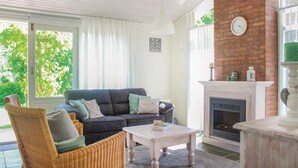 Ein gemütliches Wohnzimmer mit einem dunkelgrauen Sofa, einem Korbstuhl, einem weißen Couchtisch und einem Kamin.