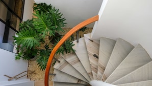 A spiral staircase with wooden steps and a curved handrail, surrounded by greenery and a white wall. - Múcura Hotel & Spa (Cartagena)