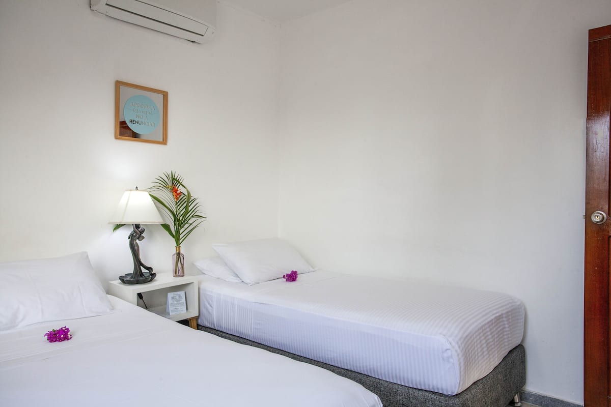 Een hotelkamer met twee enkele bedden, een nachtkastje met een lamp, een kleine plant en een ingelijst citaat aan de muur.