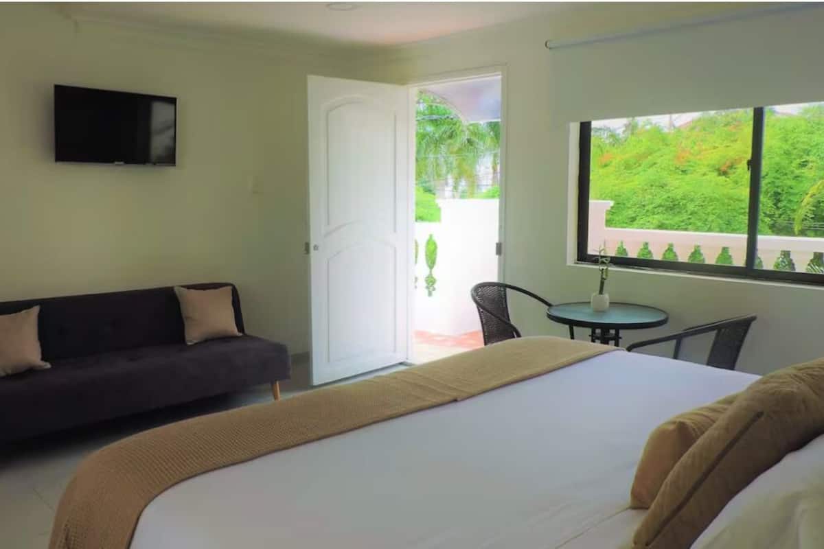 Hotelkamer met een bed, een bank, een televisie, een klein tafeltje en een raam met uitzicht op groen.