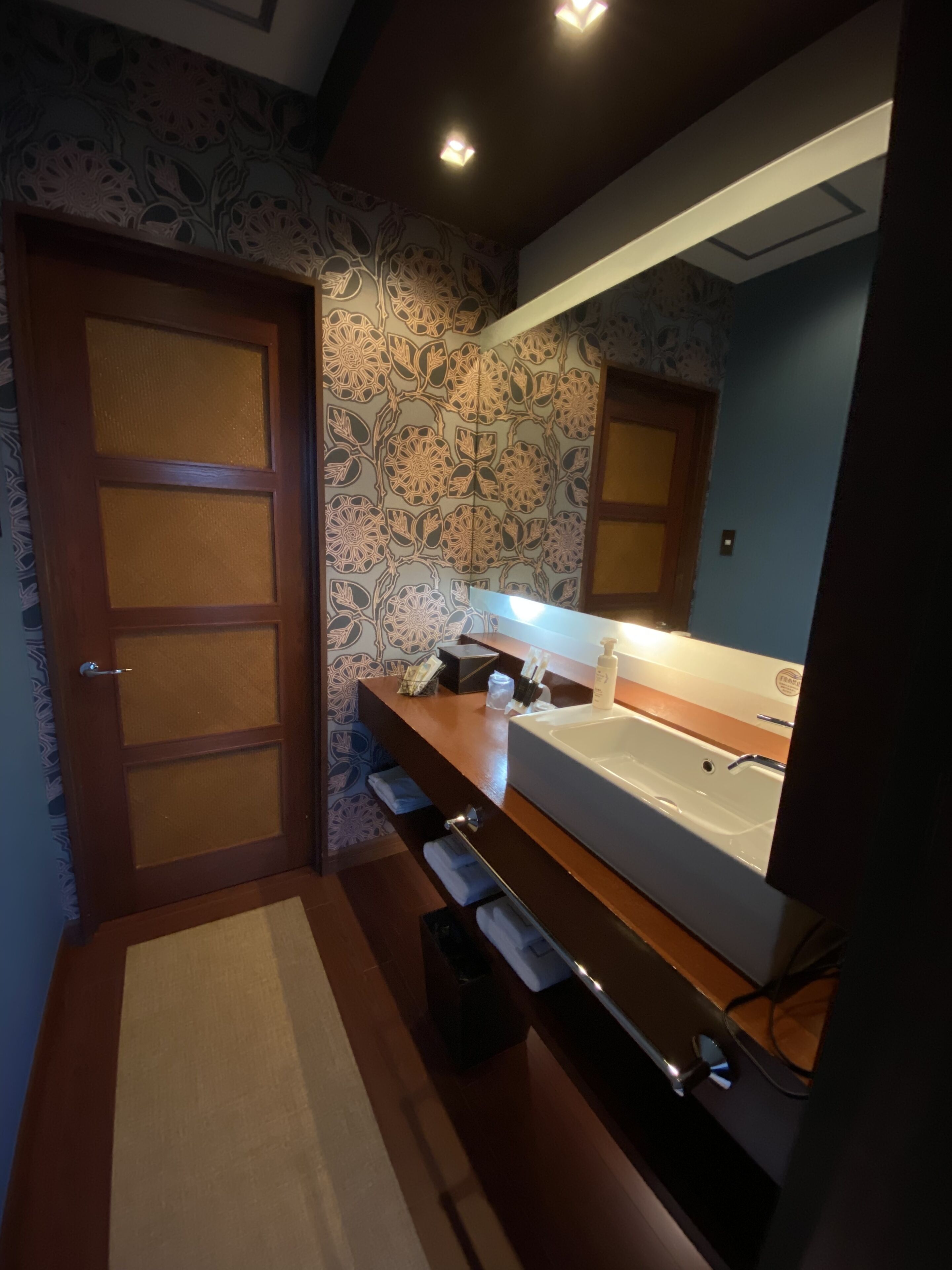 Een moderne badkamer met een groot bad, een houten wastafelmeubel en decoratief bloemenbehang.
