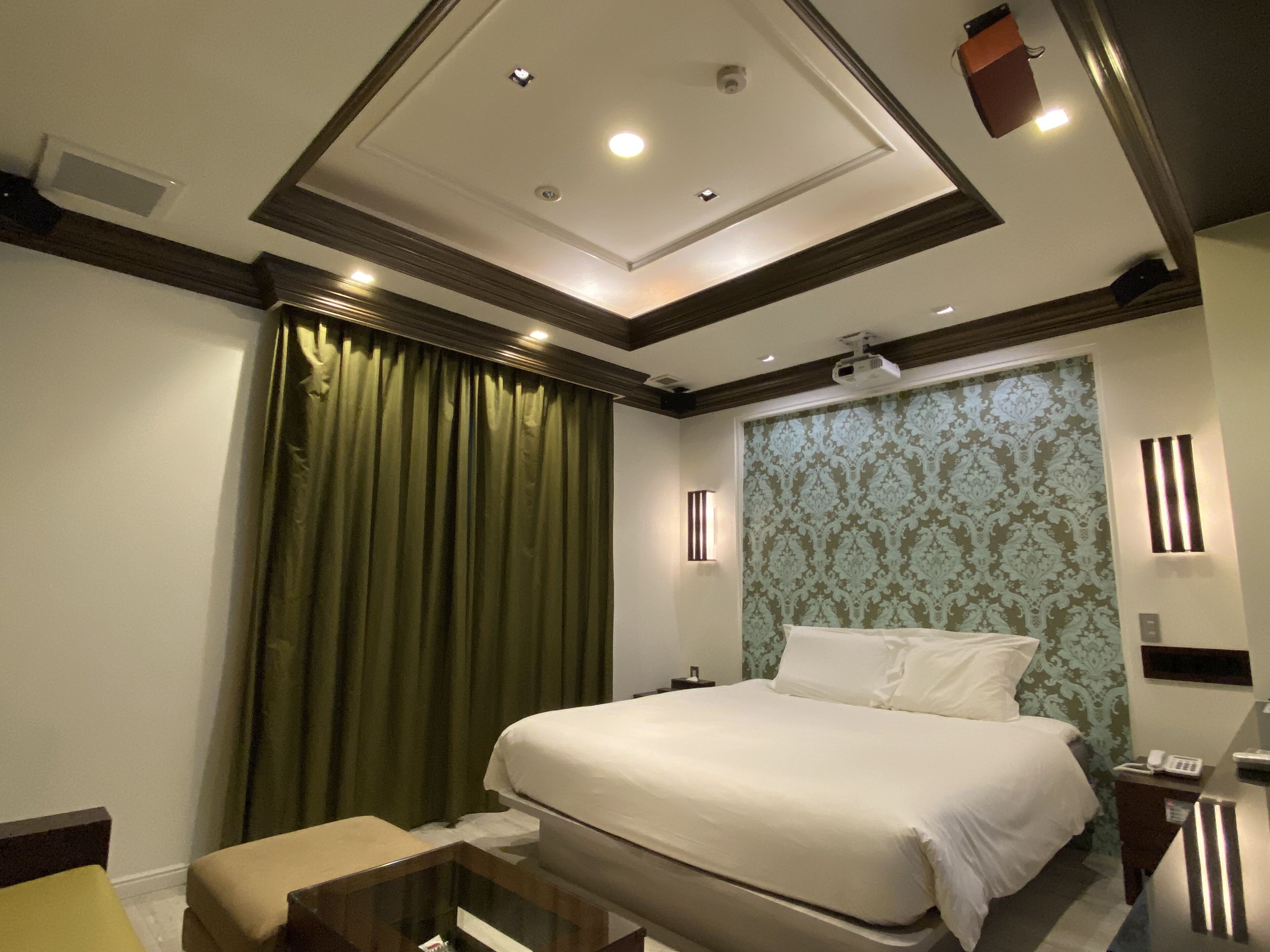 Una habitación de hotel con una cama grande, una mesita de noche, un escritorio y una cortina verde.