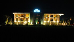 Un hôtel moderne, reconnaissable à son grand panneau « HÔTEL OASIS », qui se distingue par sa façade symétrique, dotée de nombreuses fenêtres et d’une entrée centrale.