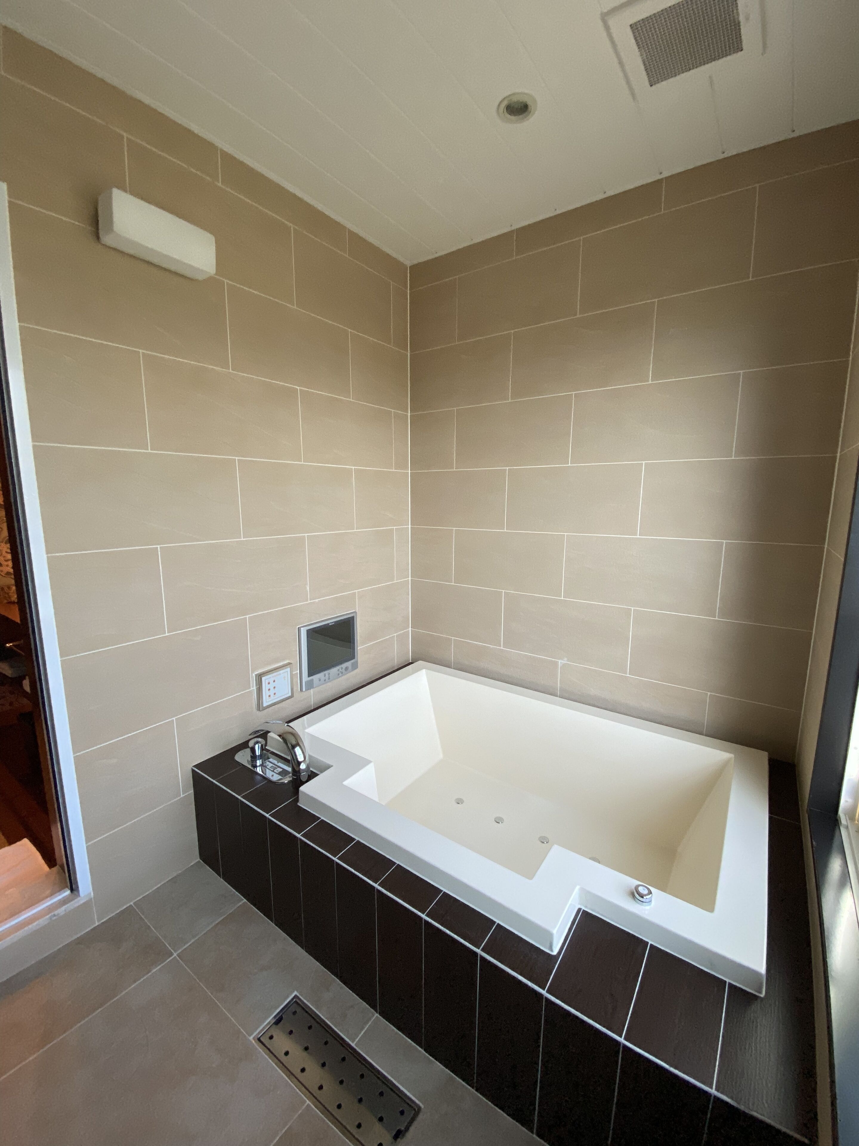 A modern bathroom with a freestanding bathtub, beige tiled walls, and a black tiled base.