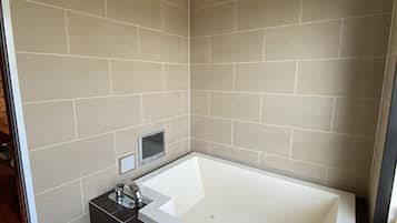 A modern bathroom with a freestanding bathtub, beige tiled walls, and a black tiled base.