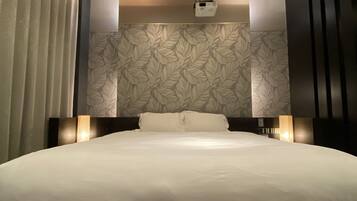 A modern hotel room with a large bed, a ceiling light, and a wall-mounted projector.