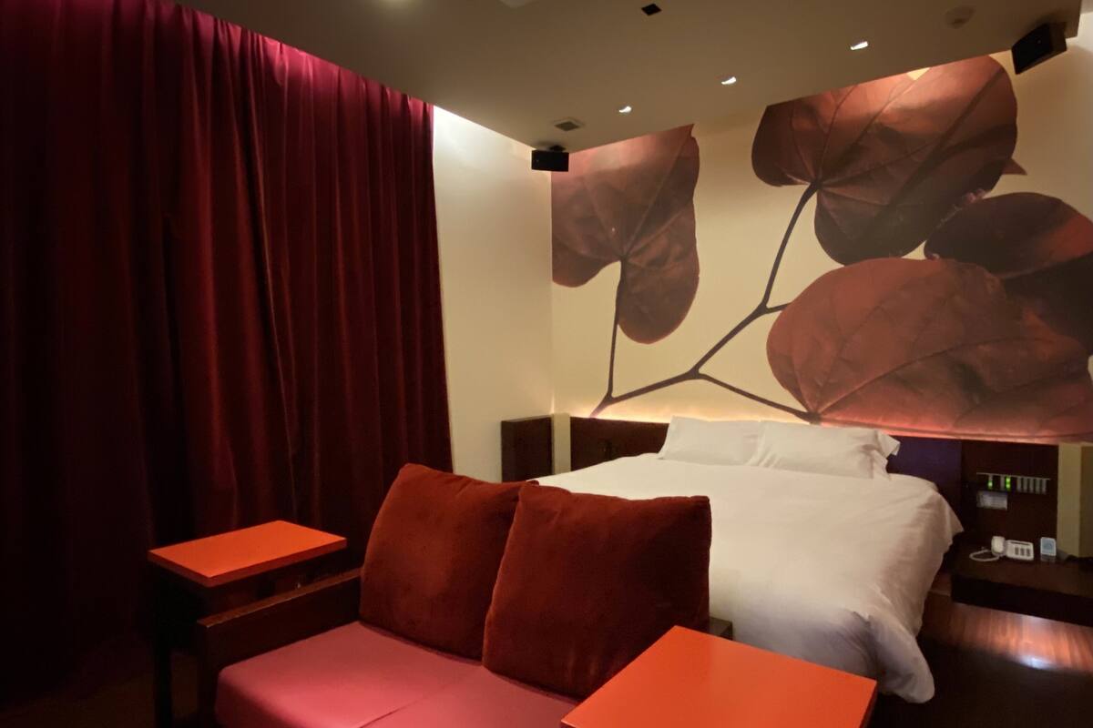 A modern hotel room with a red sofa, a small table, and a bed with white bedding.
