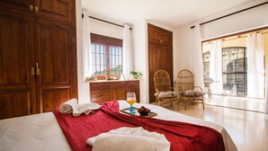A hotel room with a large bed, wooden wardrobe, a dining area with chairs, and a balcony with a view. - Villa Moskoa - PlusHolidays (Calpe)