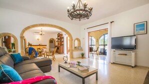 A living room with a sofa, coffee table, TV, and arched doorways. - Villa Moskoa - PlusHolidays (Calpe)