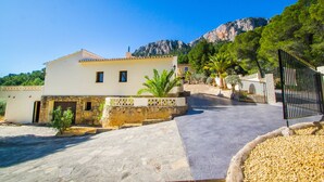 A two-story building with a stone facade, a paved driveway, and a mountain in the background. - Villa Moskoa - PlusHolidays (Calpe)