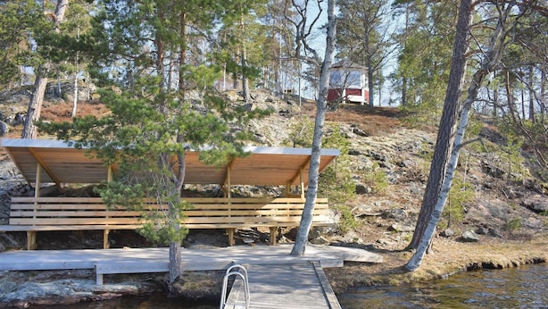 A wooden dock leading to a bench area with a shelter, surrounded by trees and a rocky hillside.