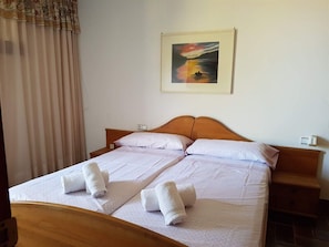 A double bed with white linens and two towels, a wooden headboard, a nightstand, and a painting on the wall.