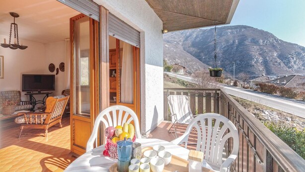 Un balcón con una mesa lista para comer, sillas, un televisor y vistas a un paisaje montañoso.