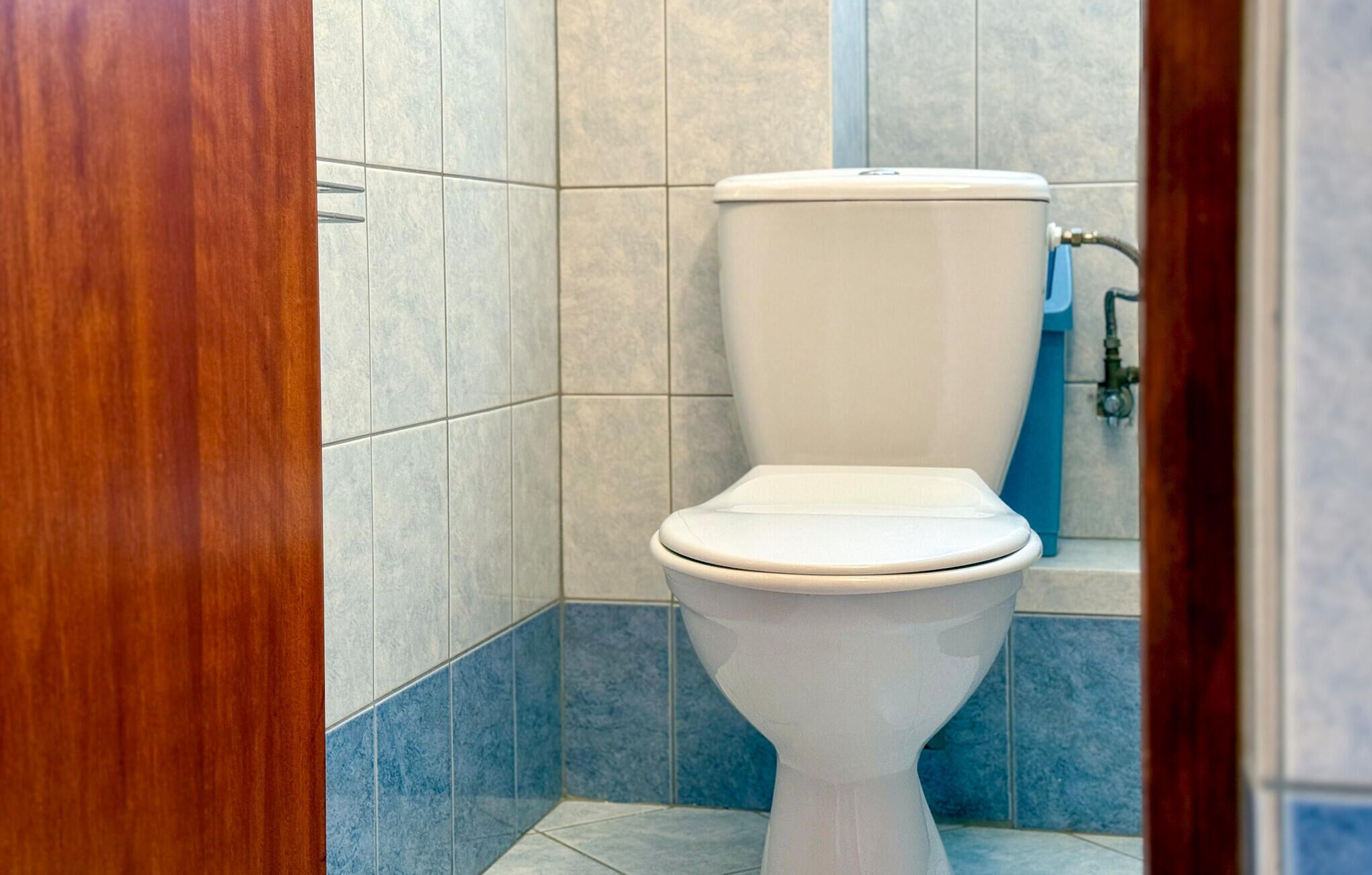 A bathroom with a white toilet, tiled walls, and a wooden door frame.