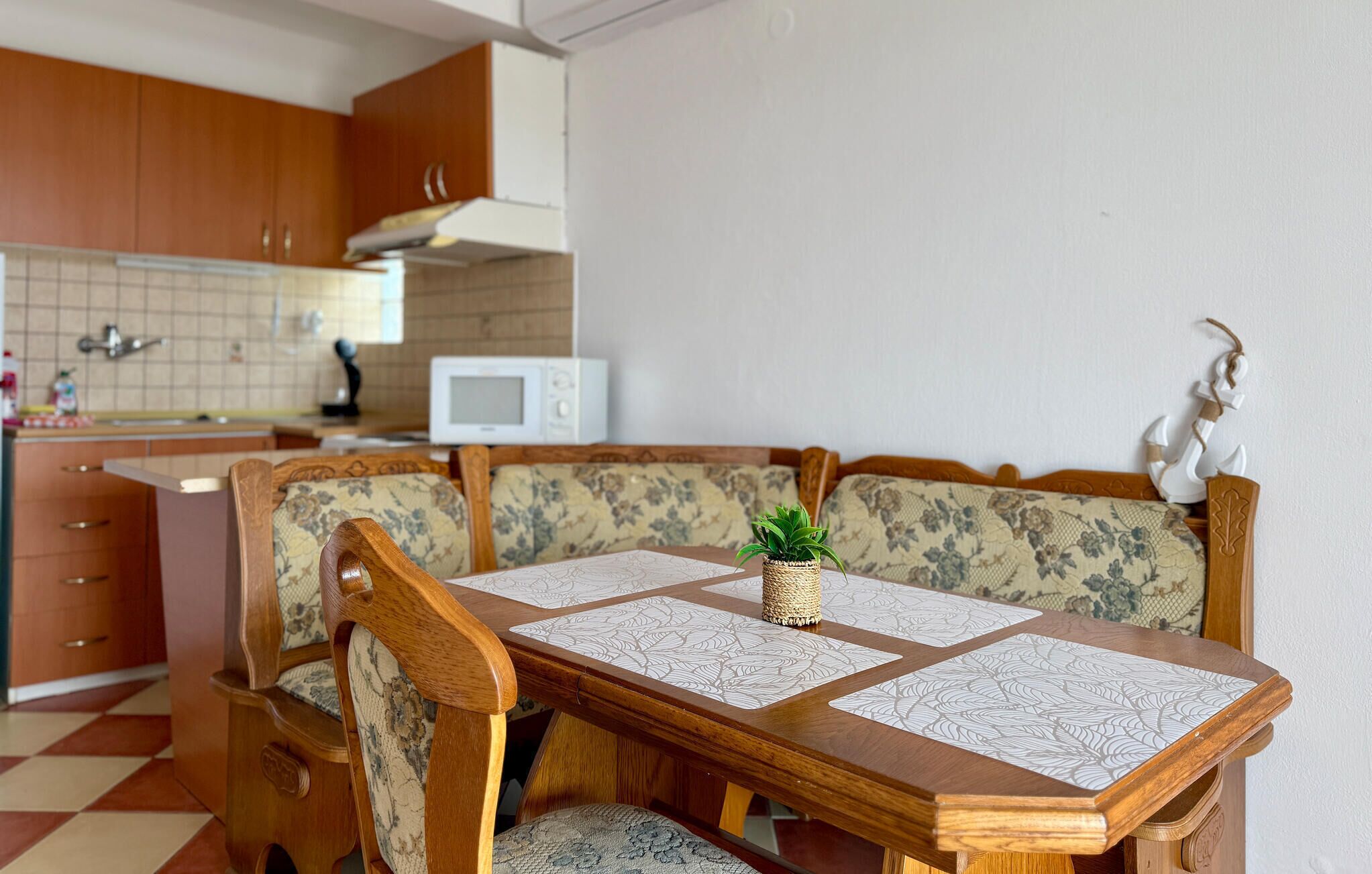 A dining area with a wooden table and chairs, a small potted plant, and a kitchen in the background.