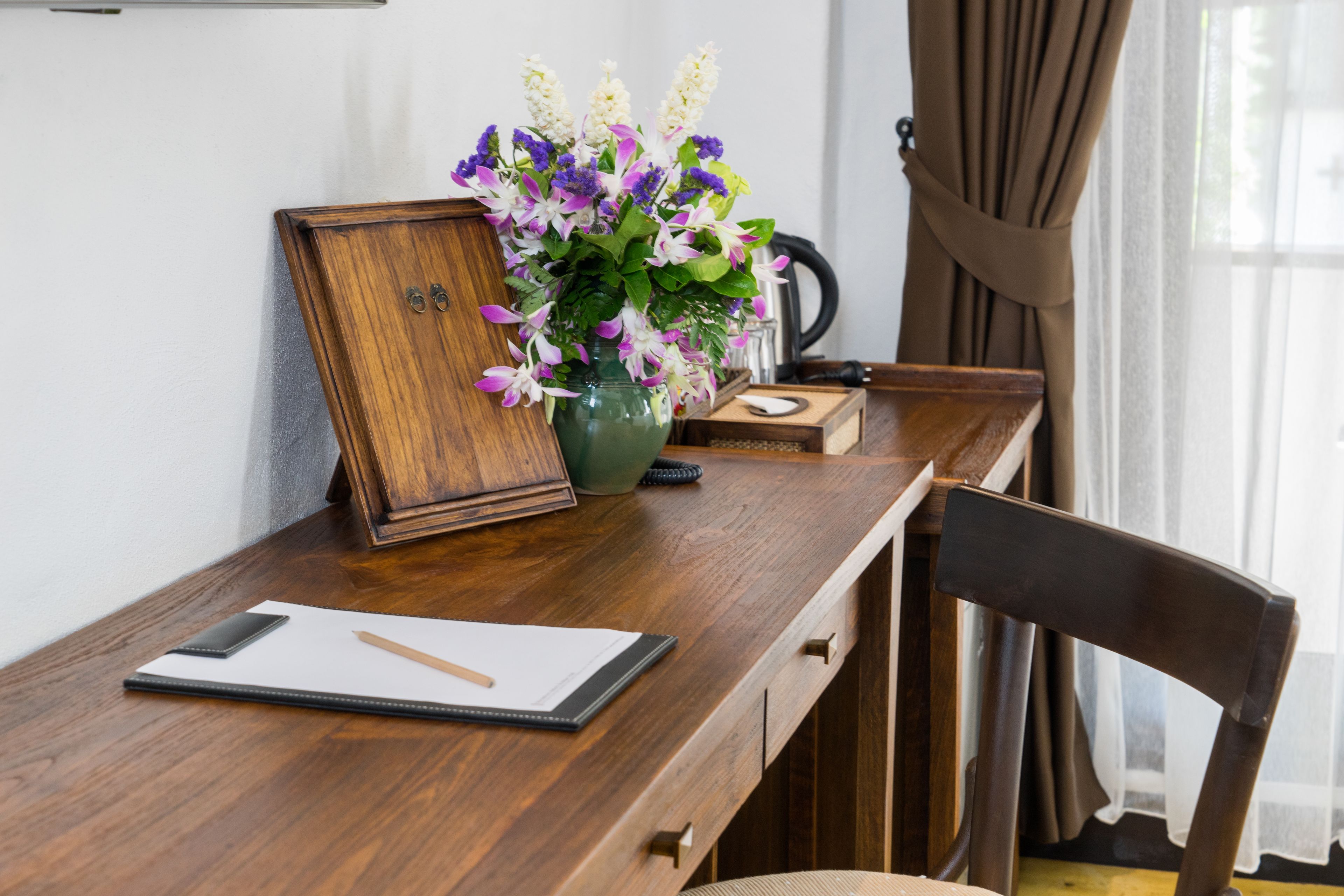 A wooden desk with a vase of flowers, a framed picture, and a smartphone.