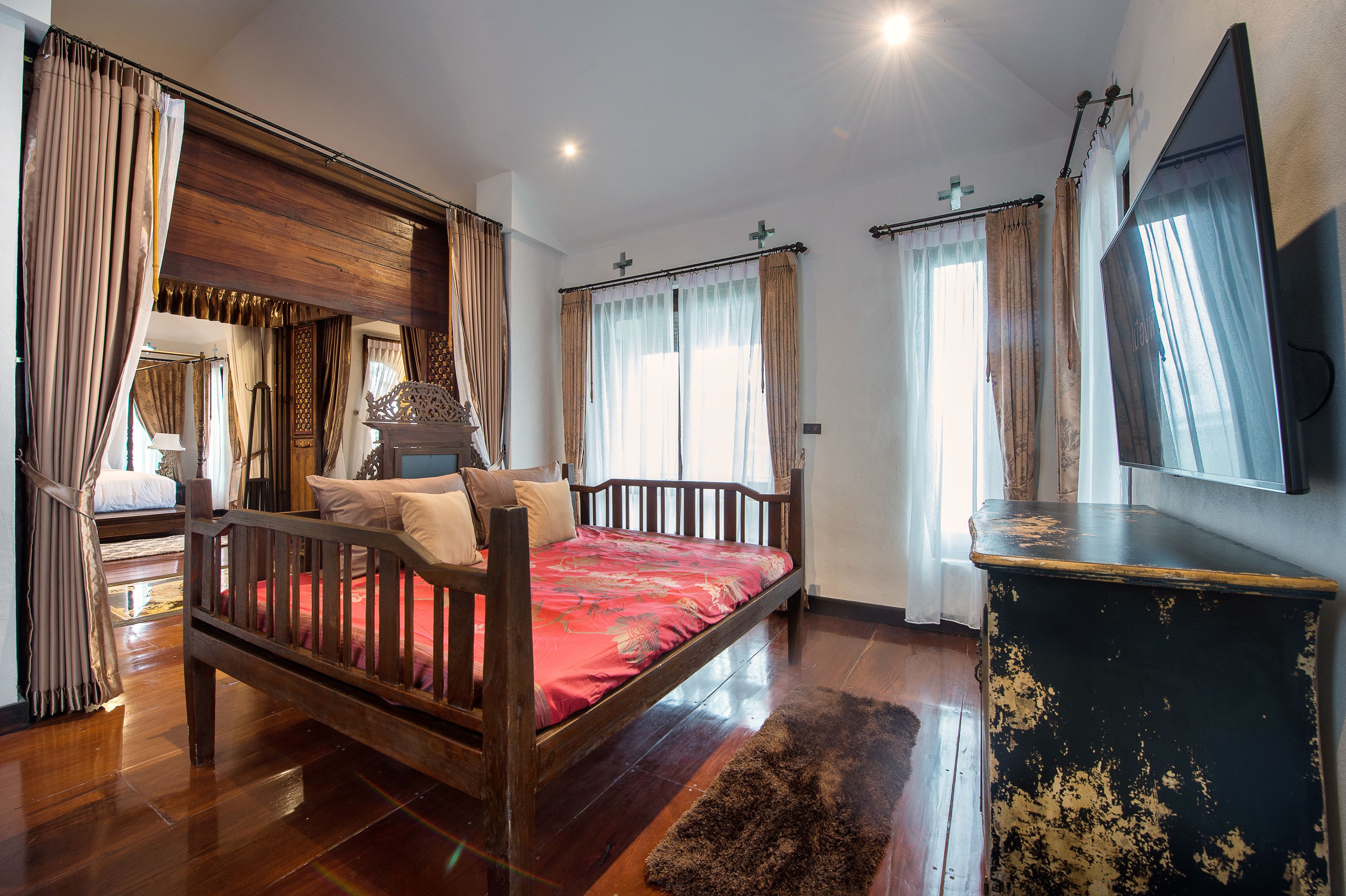 A bedroom with a wooden bed, a large mirror, and a TV on a black dresser.