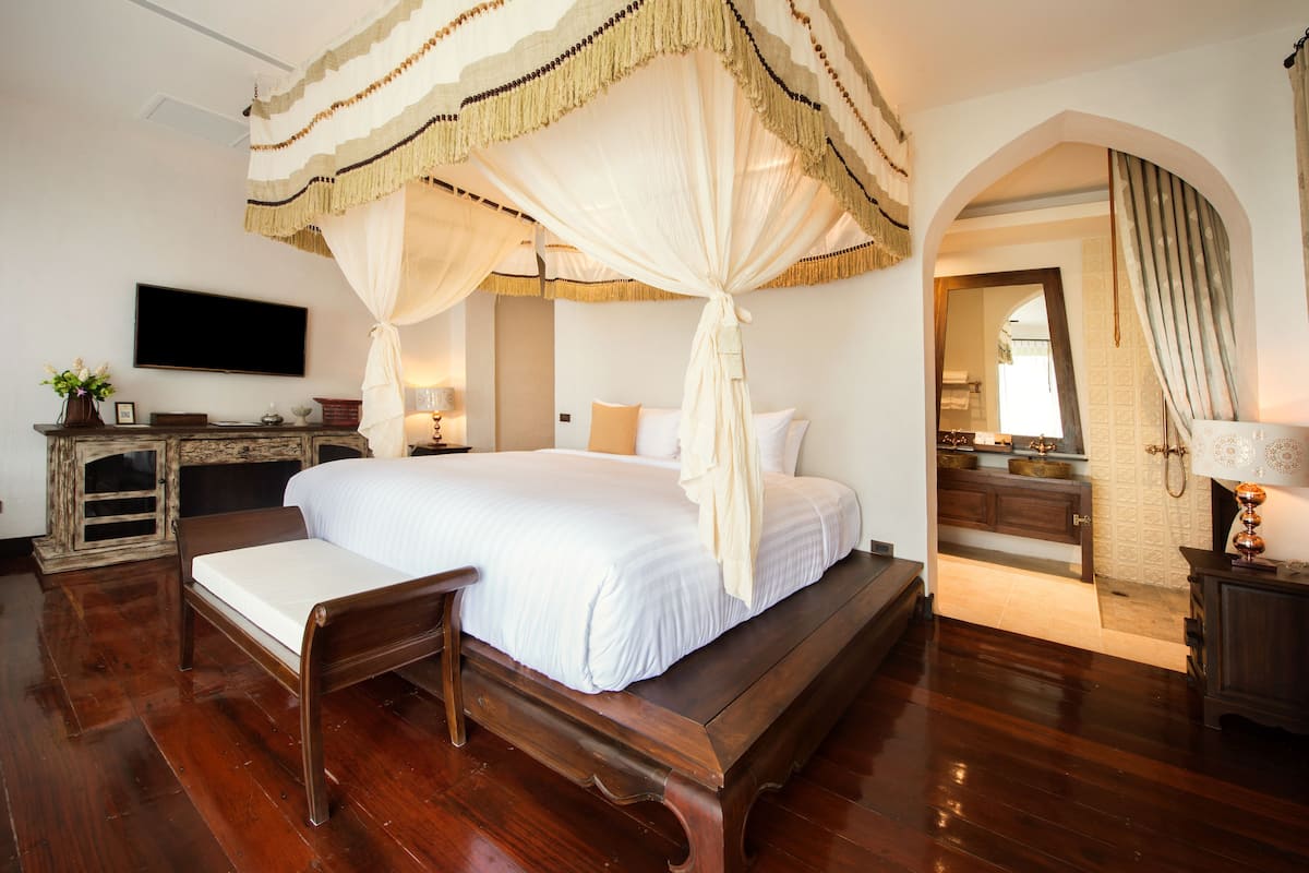 A spacious bedroom with a large bed, a wooden bench, and a TV mounted on the wall.