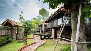A rustic wooden building with a brick pathway leading to it, surrounded by greenery and a wooden fence. - Shinnabhura Historic Boutique hotel (Phitsanulok)