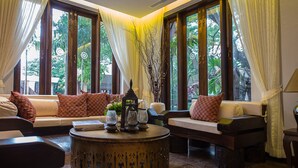 A cozy living area with a sofa set, a coffee table, and large windows with curtains. - Shinnabhura Historic Boutique hotel (Phitsanulok)