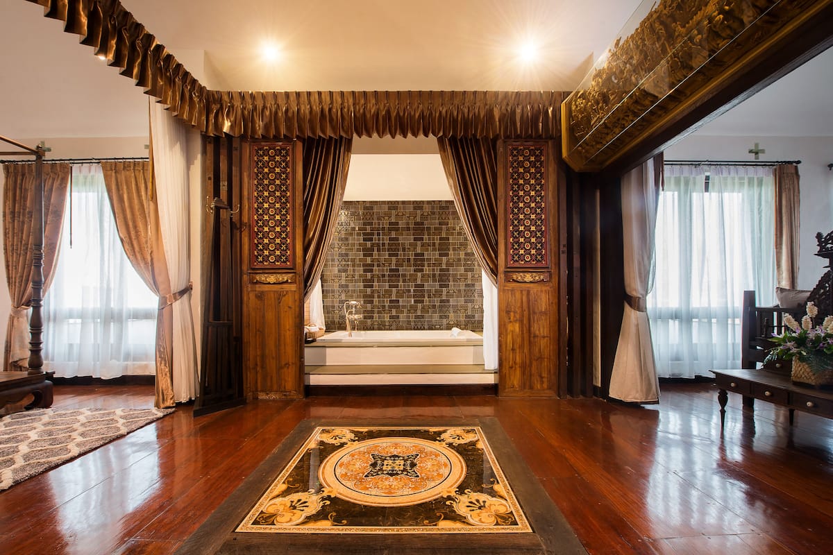 A spacious room with a large bathtub, wooden flooring, and a decorative rug.
