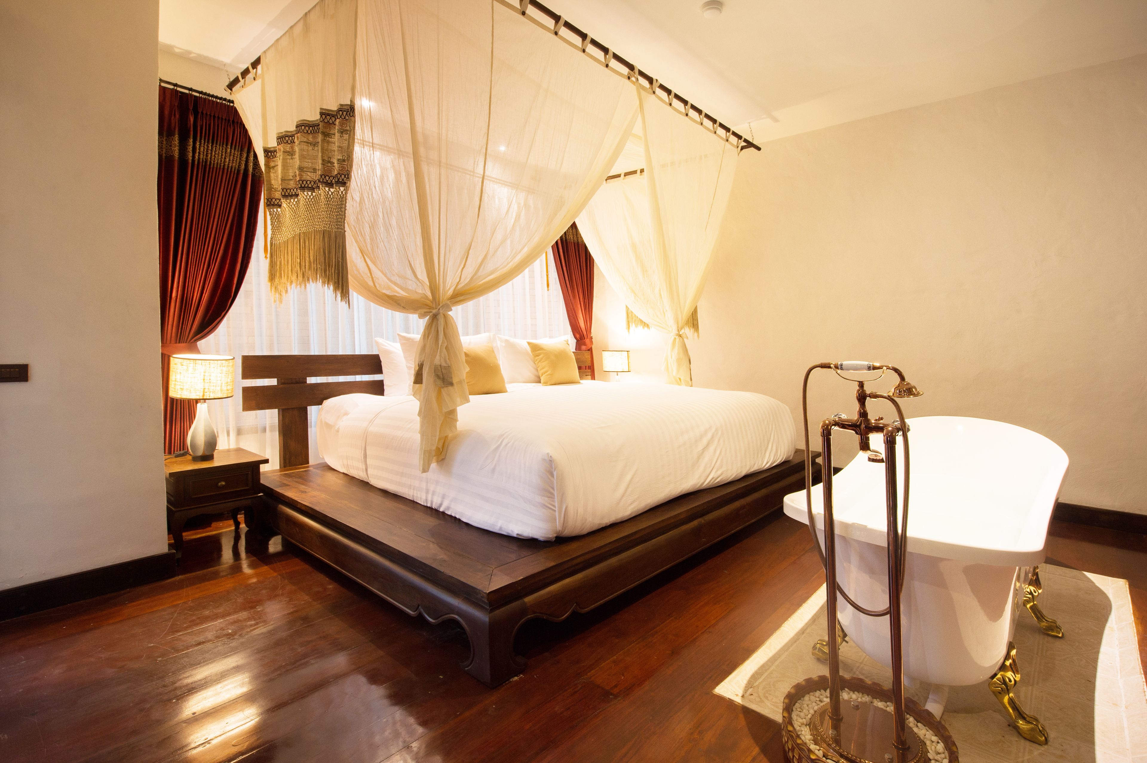 A bedroom with a four-poster bed, a white bathtub, and a wooden floor.