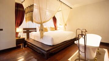 A bedroom with a four-poster bed, a white bathtub, and a wooden floor.