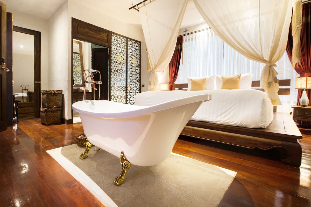 A bedroom with a large bed, a bathtub, and a wooden floor.
