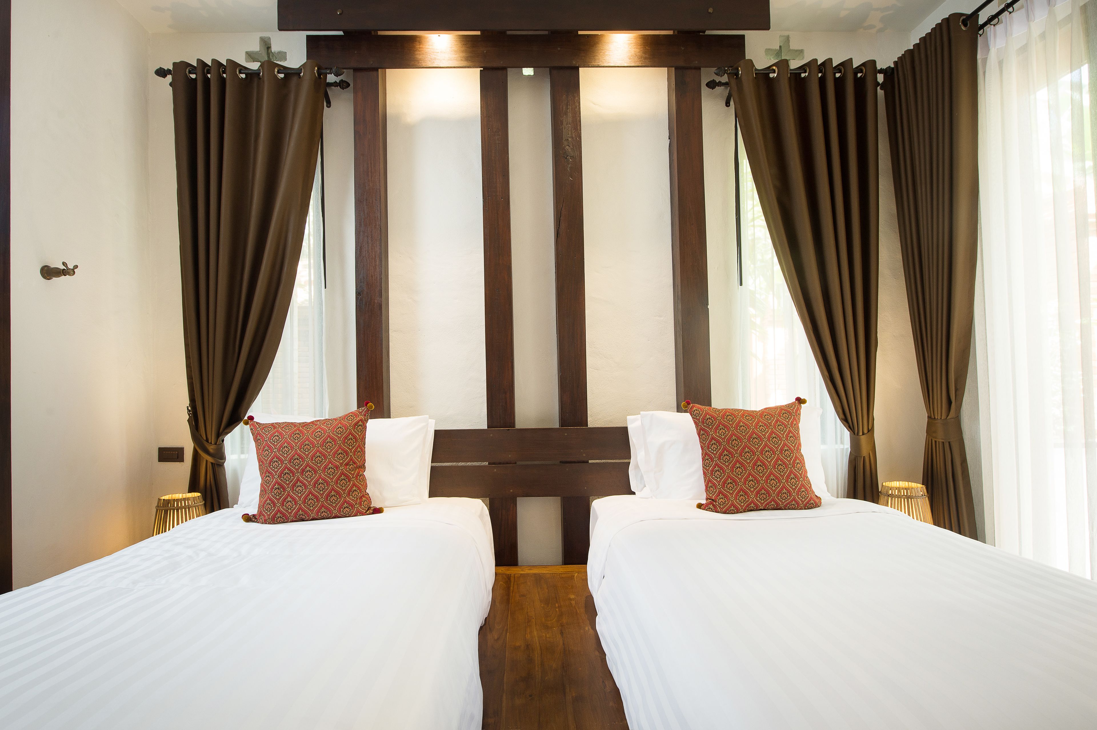 A hotel room with two beds, wooden headboard, brown curtains, white bedding, and a small side table.
