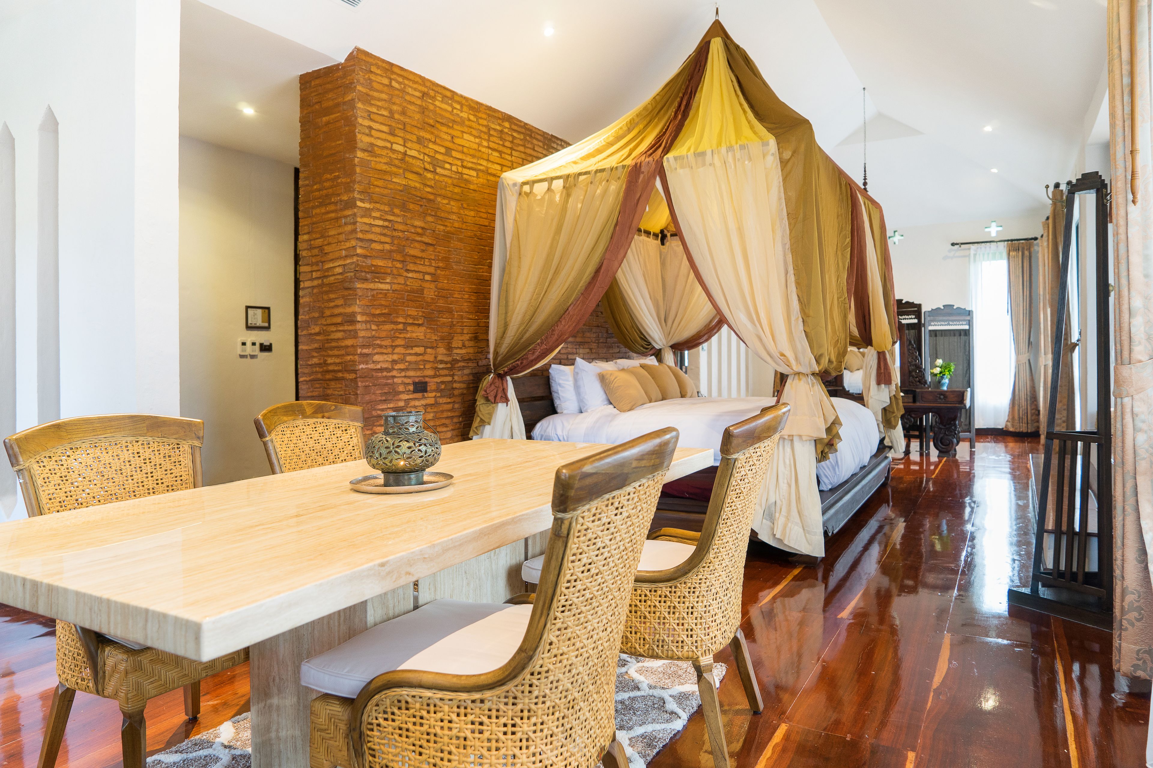 A room with a bed under a canopy, a dining table with chairs, and a brick wall.