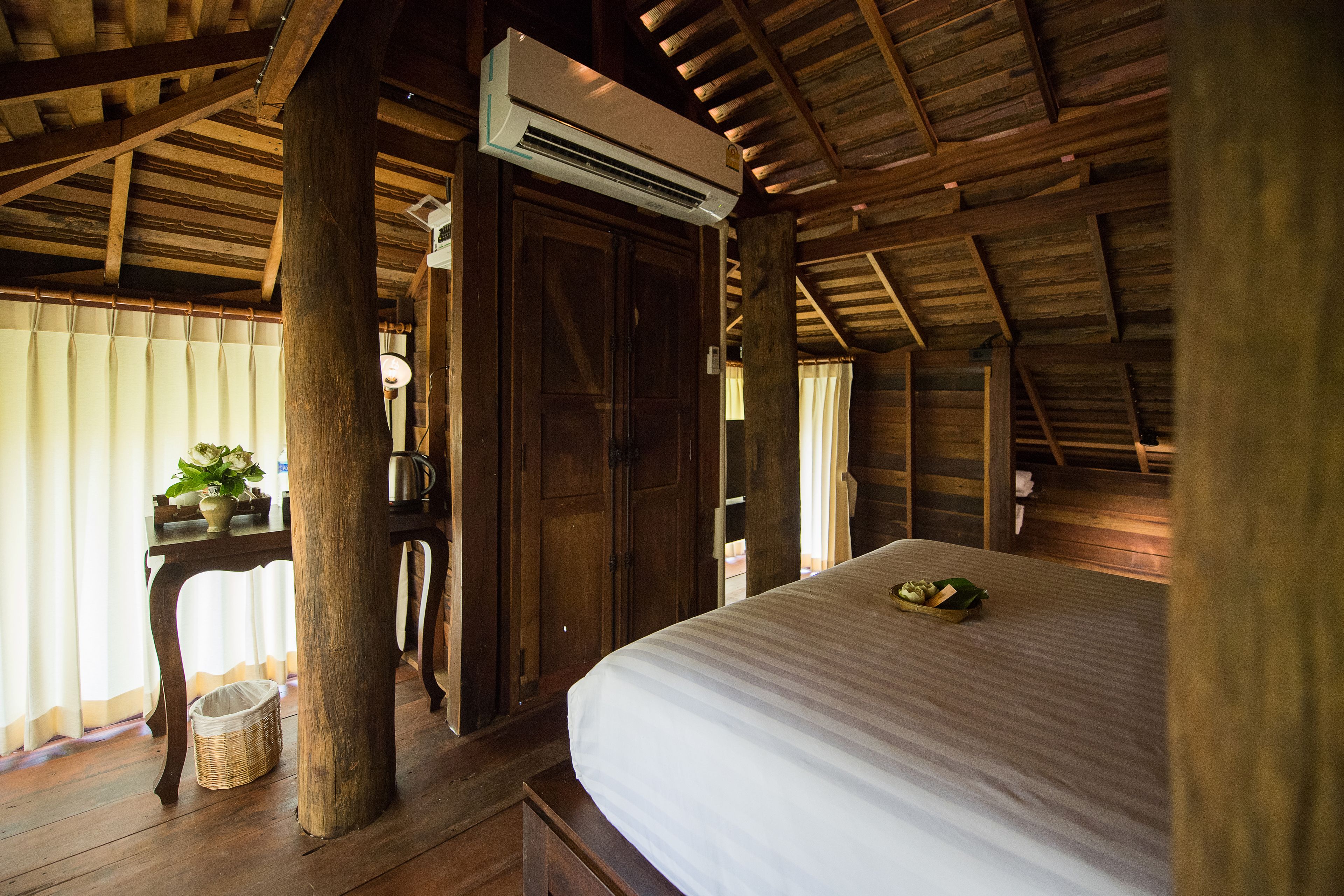 A wooden cabin bedroom with a bed, a table with a plant, and a basket on the floor.
