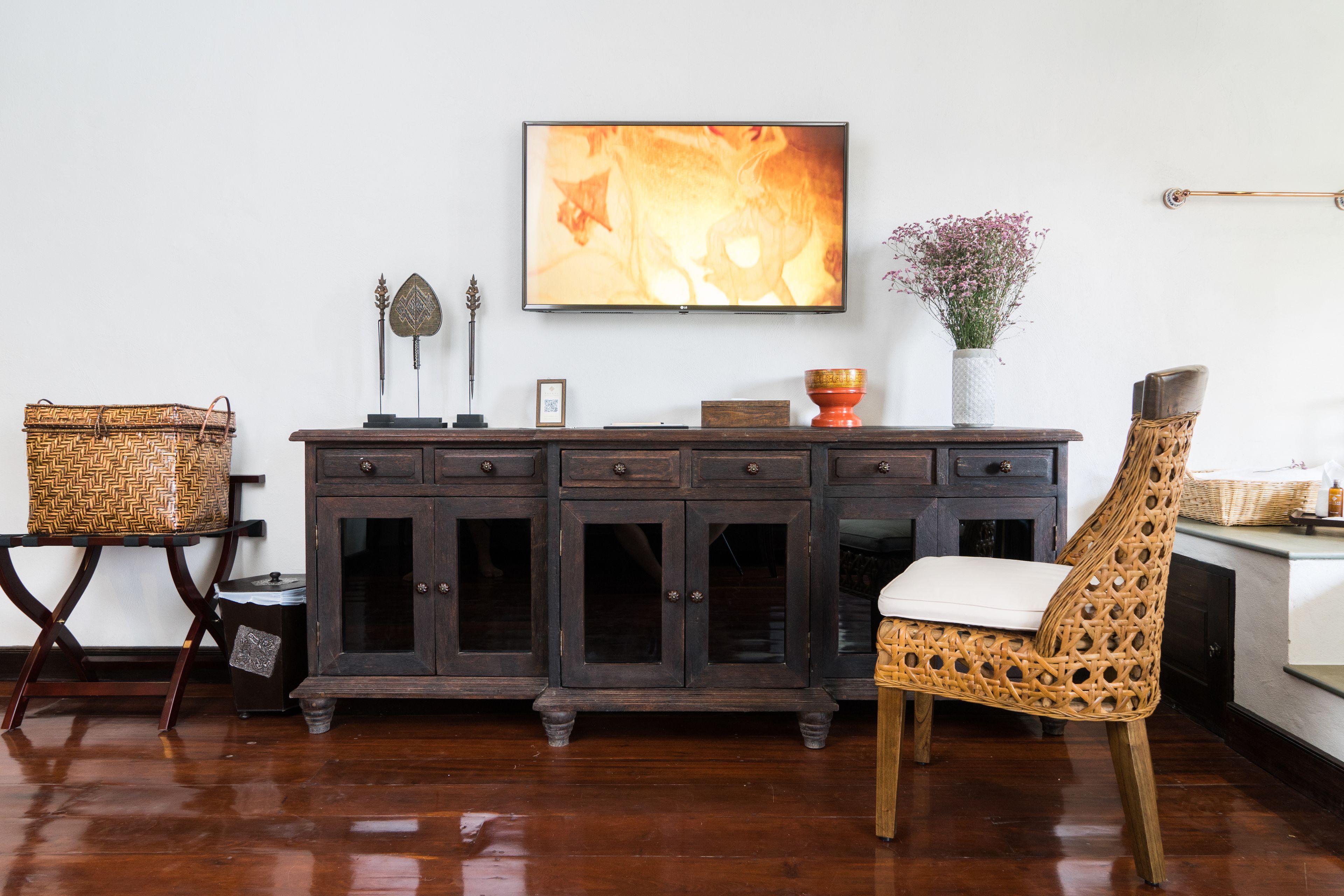 A wooden cabinet with multiple drawers, a wicker chair with a white cushion, and a framed picture on the wall.