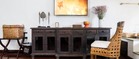 A wooden cabinet with multiple drawers, a wicker chair with a white cushion, and a framed picture on the wall.