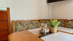 Ein Holztisch mit einer Fernbedienung, einem Glasbehälter voller Muscheln und einem Spielzeuganker sowie einem kleinen Topfpflanzen auf einem floralen Kissen.