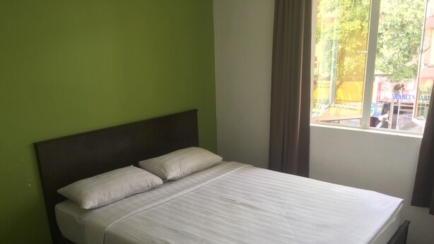 A single-bed room with a dark headboard, white bedding, and a window with curtains.