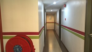 A hallway with a red fire hydrant, beige walls with red and green stripes, and a tiled floor.