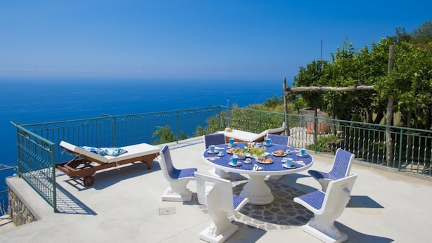 Una terraza con mesa dispuesta para comer, sillas de descanso y vistas al mar.