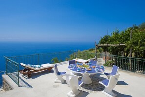 Una terraza con mesa dispuesta para comer, sillas de descanso y vistas al mar.